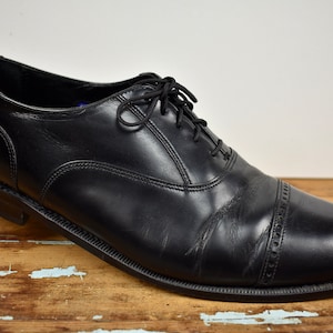 Może przedstawiać: Czarne skórzane buty wiązane z noskiem typu cap toe.