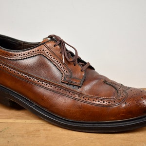May include: Brown leather brogue shoes with a lace-up closure. The shoes have a wingtip design and a black rubber sole.