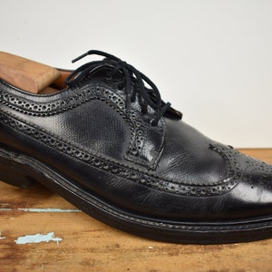 May include: Black leather lace-up shoes with wingtip detailing. The shoes have a brogue pattern and a rounded toe.