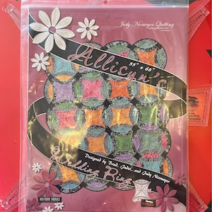 Peut inclure: Un modèle de quilting pour une courtepointe en forme d'anneau de mariage, conçu par Brad, Judel et Judy Niemeyer. Le modèle s'appelle "Allyson's Wedding Ring" et mesure 140 cm sur 173 cm. Le modèle présente un design de courtepointe coloré avec une variété de tissus.