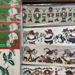 May include: A set of iron-on patches featuring Christmas themes. The patches include nutcrackers, Santa Claus, rocking horses, and holly leaves. The patches are packaged in clear plastic bags with the words "Glitterlooks" and "Instant Iron-On Fashion Accents" printed on them.