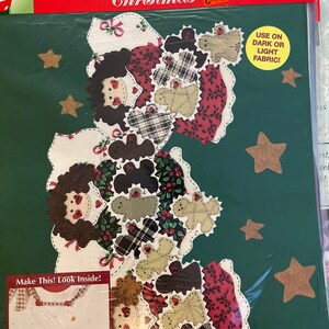 May include: Iron-on transfer sheet with a Christmas theme featuring a group of patchwork dolls and stars. The sheet is packaged in a clear plastic sleeve with the text "Iron-on Transfer Christmas" and "Use on dark or light fabric!" printed on it.