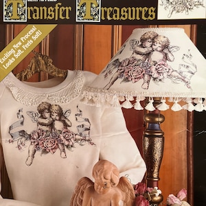 May include: A cream-colored sweatshirt with a lace collar and a heat-applied angel graphic. The image also shows a matching lampshade with a similar angel design, a small angel figurine, and the "DAISY KINGDOM Transfer Treasures" packaging.