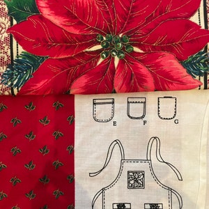 May include: A fabric panel featuring a large red poinsettia print at the top, a red section with small green holly leaves, and a white section with black line drawings of an apron and three pocket styles labeled E, F, and G for sewing projects.