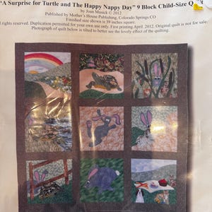 Op de afbeelding: Een quiltblokpatroon met een patchwork-ontwerp met een schildpad, konijnen en een picknickscène. Het quiltblok is 39 inch vierkant en heeft de titel "A Surprise for Turtle and The Happy Nappy Day".
