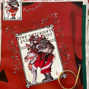 May include: Iron-on transfer featuring a vintage illustration of Santa Claus carrying a bag of gifts and a child. The illustration is surrounded by a white border and the text "The Saturday Eve Post" is printed above and below the image. The transfer is on a red background with a gold horn in the lower right corner.