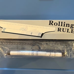 Puede incluir: Un paquete de plástico transparente que contiene una regla de rodillo plateada con un transportador y una hoja de instrucciones en blanco y negro. El paquete está etiquetado como "Rolling Ruler".