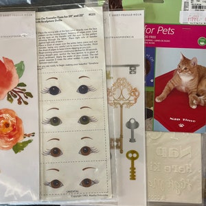 Puede incluir: Un conjunto de hojas de transferencia termoadhesivas para manualidades. Las hojas presentan una variedad de diseños, incluyendo flores, llaves y ojos. Las hojas están empaquetadas en fundas de plástico transparente y etiquetadas con el nombre de la marca "Iron-it Out".