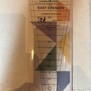Puede incluir: Una regla de plástico transparente con marcas para cortar bloques de acolchado Dresden. La regla está etiquetada como "Easy Dresden" e incluye el texto "Pattern Enclosed!" y "Cuts accurate wedges every time!" La regla mide 8 pulgadas de largo y tiene marcas para incrementos de 1/2 pulgada.