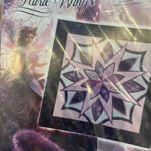 May include: A package featuring a quilt pattern with the text "Fairie Wings" and "Timeless Treasures." The quilt design is a starburst pattern in shades of purple and pink. A picture of a fairy is also visible.