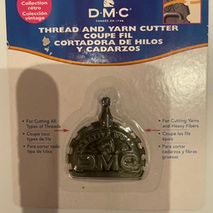 May include: DMC Creative Works thread and yarn cutter, a silver-toned metal tool with a serrated edge, packaged on a white card with the text "THREAD AND YARN CUTTER COUPE FIL CORTADORA DE HILOS Y CADARZOS" in black and red.