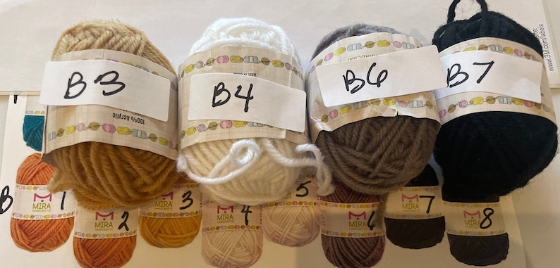 May include: Four balls of yarn in different colors: beige, white, gray, and black. Each ball has a label with a letter and number, B3, B4, B6, and B7.