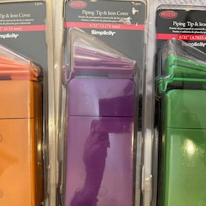 May include: Three packages of piping tip and iron covers in orange, purple, and green. Each package contains two covers and is labeled with the size in inches and millimeters. The packages are labeled "Simplicity".