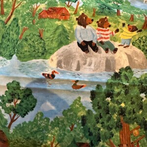 May include: Three brown bears sitting on a large rock by a blue river. The bears are wearing clothes. The bear on the left is wearing a blue shirt and brown pants. The bear in the middle is wearing a red and white striped shirt and blue pants. The bear on the right is wearing a yellow shirt and brown pants. There is a small red house in the background.