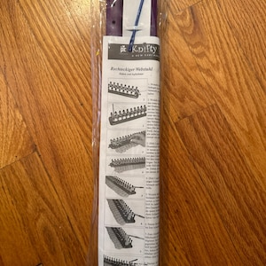 Puede incluir: Telar de tejido de plástico morado con instrucciones de uso. Las instrucciones están en alemán e incluyen el texto "Rechteckiger Webstuhl" que se traduce como "Telar rectangular".