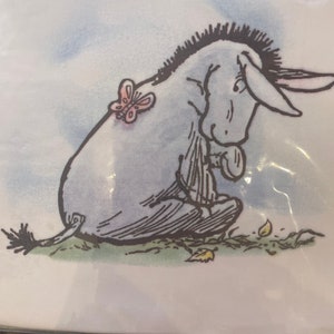 May include: A black and white illustration of a sad donkey with a pink butterfly on its back. The donkey is sitting on a green patch of grass with brown leaves scattered around it.