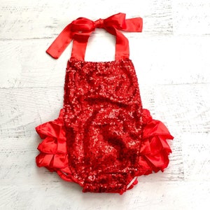 May include: Red sequined baby romper with a red satin bow and ruffled trim.