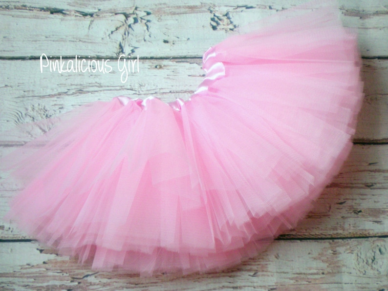 K&ouml;nnte beinhalten: Ein rosa T&uuml;ll-Tutu mit einem Satin-Bund. Das Tutu ist geschichtet und flauschig, perfekt f&uuml;r ein kleines M&auml;dchen zum Verkleiden.