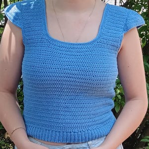 May include: A light blue crochet top with a square neckline and short, ruffled sleeves.