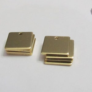 May include: A stack of five gold-colored metal square tags with a small hole in the center of each tag.