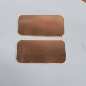 May include: Two rectangular copper plates with rounded corners. The plates have a smooth, metallic, reddish-brown surface finish and are positioned horizontally, one above the other, displaying a flat, uniform appearance without any markings.