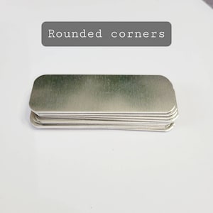 May include: A stack of silver metal name tags with rounded corners. The text "Rounded corners" is visible above the stack.