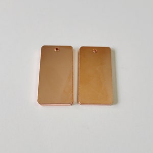 May include: Two rectangular rose gold metal tags with a hole at the top.