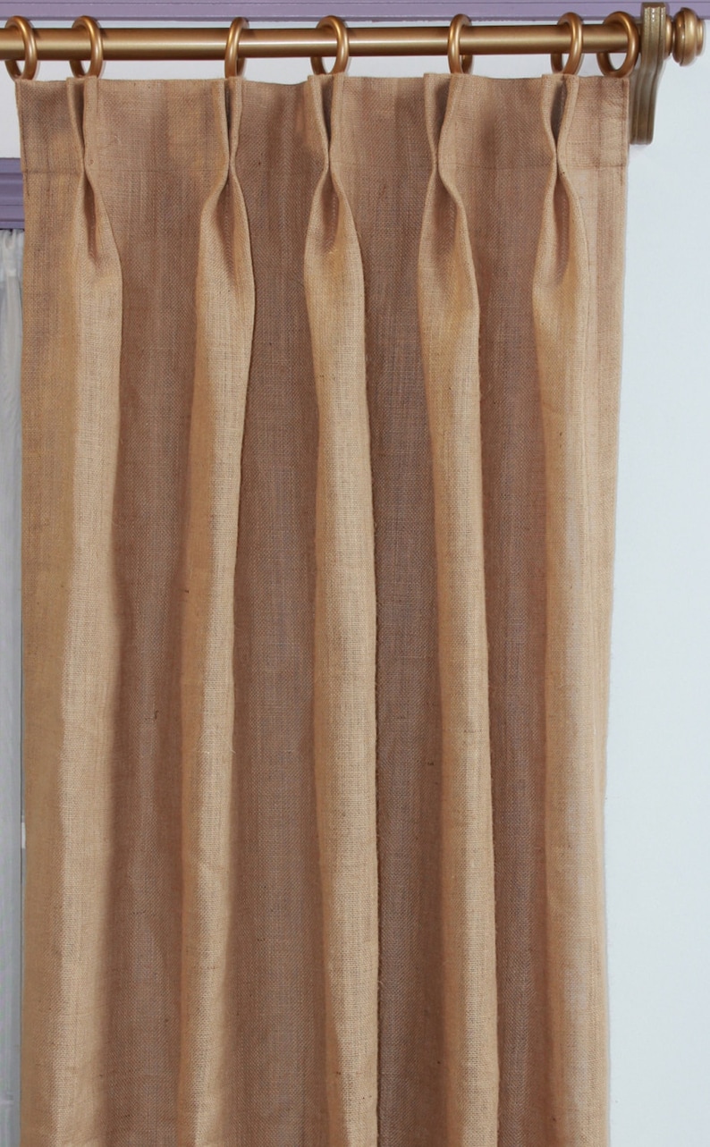 May include: A set of brown burlap curtains with pleats hanging from a gold curtain rod.
