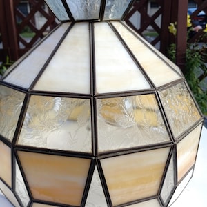 May include: A stained glass lamp shade featuring a geometric design with alternating panels of opaque cream glass and textured, clear glass with a fern-like pattern. The panels are joined by dark metal soldering, forming a wide, multi-faceted dome.