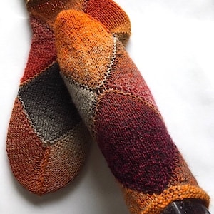 Könnte beinhalten: Ein Paar gestrickte Socken mit Patchwork-Muster in Orange-, Braun- und Rottönen. Die Socken sind aus verschiedenen Garnen gefertigt und haben einen einzigartigen, handgefertigten Look.