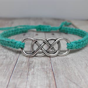 May include: A turquoise blue braided cord bracelet with a silver infinity knot charm.