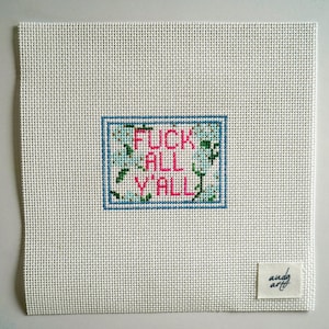 May include: A white canvas with a cross-stitched design. The design features the phrase "FUCK ALL Y'ALL" in pink and green, framed in blue. A small white tag with "andy art" is in the lower right corner.