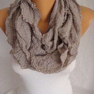 May include: A beige ruffled infinity scarf made of a soft, textured fabric.