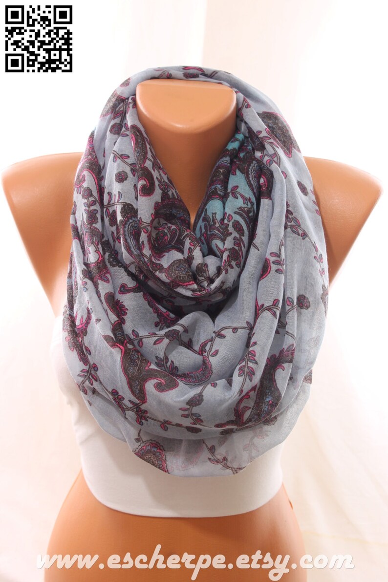 May include: A gray infinity scarf with a paisley pattern in shades of pink, blue, and black. The scarf is made of a soft, lightweight fabric.