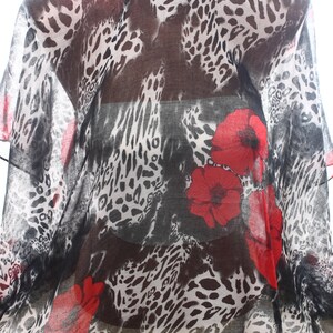 Puede incluir: Una bufanda transparente con estampado de leopardo blanco y negro y flores rojas de amapola.