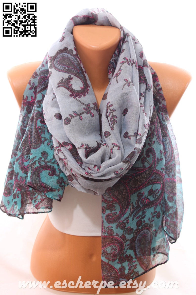May include: A gray and teal paisley patterned scarf with pink accents. The scarf is folded and draped around a mannequin's neck.