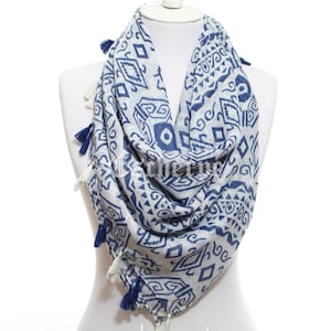 Puede incluir: Una bufanda de patrón blanco y azul con borlas blancas. La bufanda tiene un diseño geométrico con acentos azules.