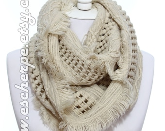 Peut inclure: Une écharpe en tricot infini de couleur crème avec une bordure à franges et un motif texturé. L'écharpe est faite d'un matériau doux et confortable, idéale pour se tenir au chaud en hiver.