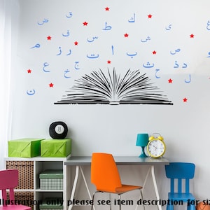 May include: A black and white illustration of an open book with blue Arabic letters and red stars surrounding it. The letters are arranged in a semi-circle shape above the book. The image is on a white wall with a bookshelf and a desk with chairs in the background.