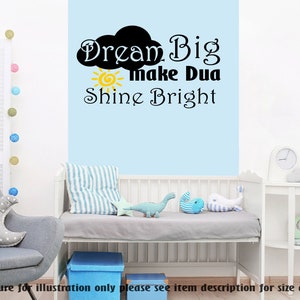 May include: A white cot with a blue and white striped mattress pad. The wall behind the cot has a black and yellow decal that reads "Dream Big make Dua Shine Bright".