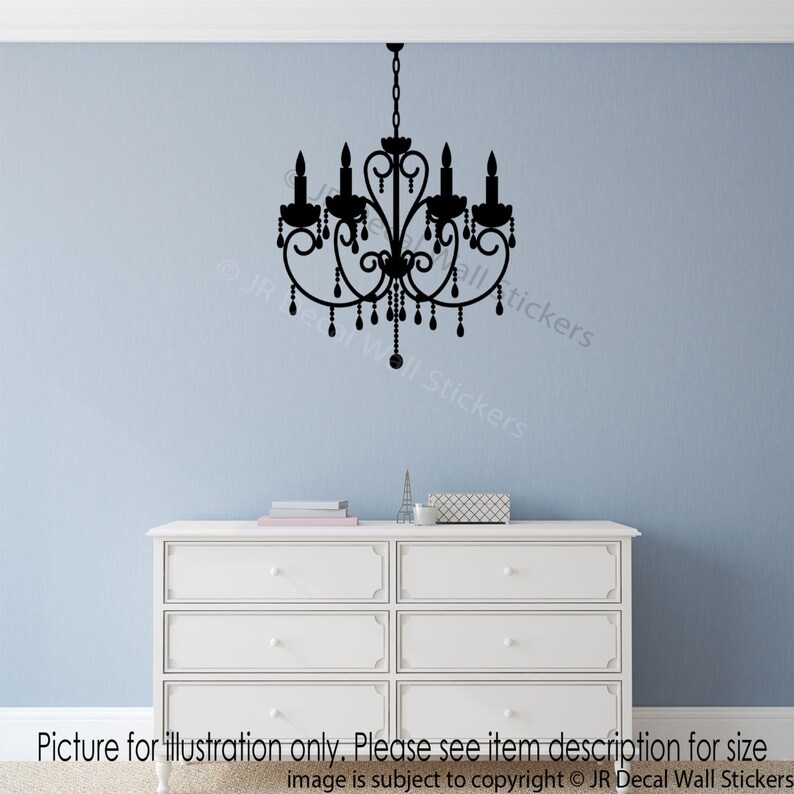 May include: Black silhouette of a chandelier with a decorative design and hanging crystals. The chandelier is on a light blue wall above a white dresser.
