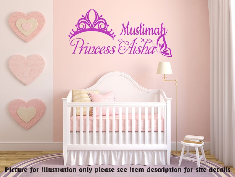 May include: Purple vinyl wall decal with a crown, butterfly, and the text "Muslimah Princess Aisha". The decal is displayed on a pink wall above a white crib with a pink and white bedding set.