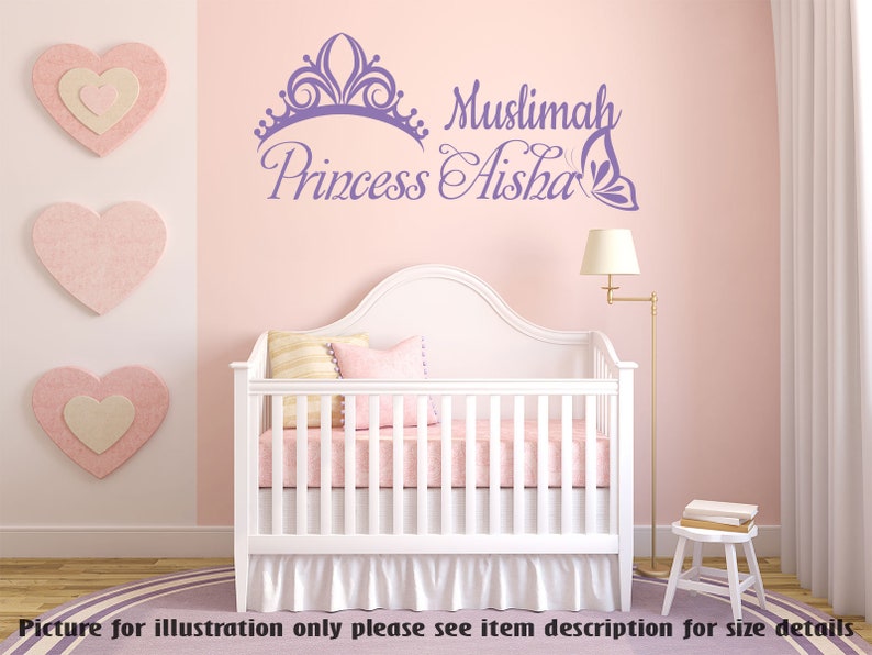 May include: Purple and white wall decal with a crown, butterfly, and the text "Muslimah Princess Aisha". The decal is on a pink wall above a white crib with a pink and white bedding set.