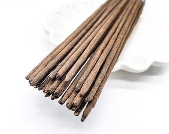 May include: A bundle of brown incense sticks with purple tips, arranged on a white plate.