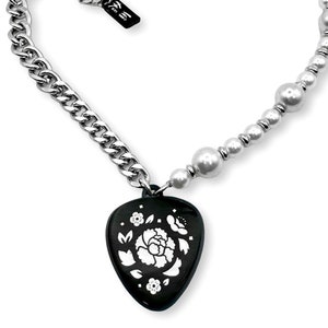 Puede incluir: Un collar plateado con un colgante negro con un diseño floral blanco. El collar combina una cadena gruesa con un collar de perlas. El colgante tiene forma de corazón y tiene un acabado brillante.