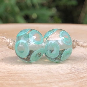 Two artisanal flame-spun glass beads, transparent, green, gray