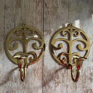 May include: Two gold metal wall sconces with a decorative tree design and a candle holder on each side.