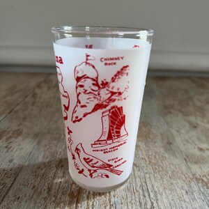 May include: A clear glass tumbler with a white background and red illustrations. The tumbler features images of Chimney Rock, Wright Memorial Beacon, and a cardinal. The text "na" is visible on the side.