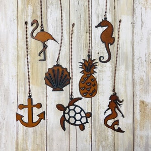 May include: A set of eight metal hanging ornaments with a nautical and tropical theme. The ornaments are in the shape of a flamingo, seashell, pineapple, seahorse, anchor, turtle, and mermaid. The ornaments are all rusty brown in color and are hanging from copper chains.