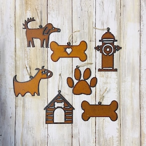 May include: Seven rustic metal ornaments in the shape of a dog, bone, paw print, doghouse, and fire hydrant. The ornaments are painted in a brown color with white accents.